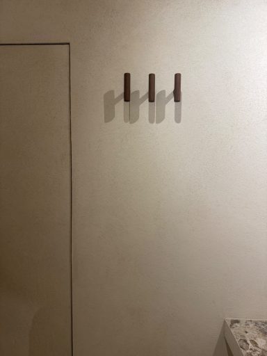 Drie houten kledinghangers aan een lichte muur.