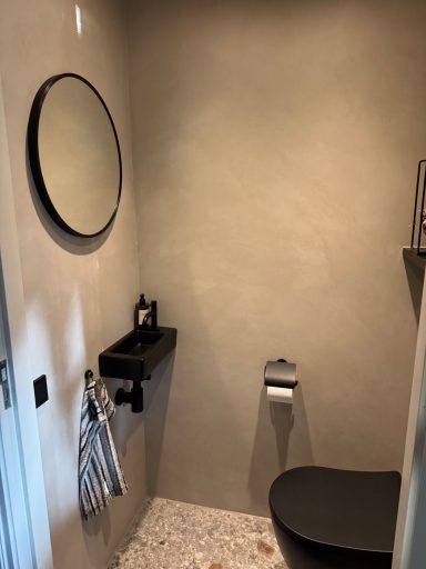 Moderne toiletruimte met ronde spiegel, zwarte wastafel en minimalistische inrichting.