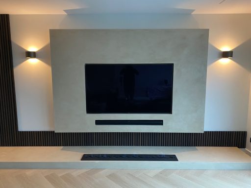 Moderne woonkamer met een wand-tv, omgeven door sfeerverlichting en een houten plint.